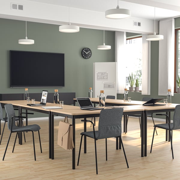 Moderne groene vergaderruimte met groot scherm, houten tafels en LÄKTARE-stoelen. Hanglampen, klok en ramen met jaloezieën.
