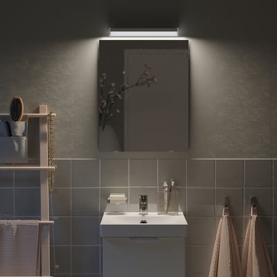 Kleine, grijze LÄRBRO spiegel in de badkamer, verlicht boven witte wastafel, omgeven door donkere tegels.