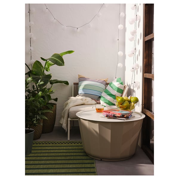 Moderne buitenhoek met witte LÅGASKÄR tafel, gestreepte kussens, groen vloerkleed, grote plant en hanglampen.