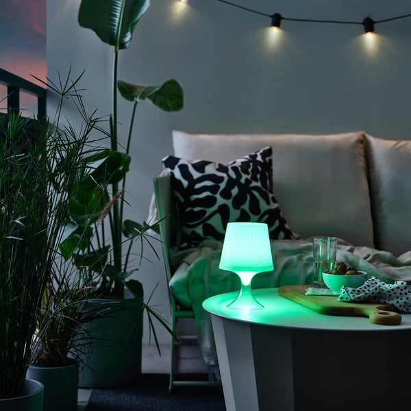 Kleine groene LAMPAN-lamp op tafel met planten en bank in de schemering.