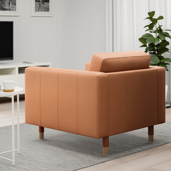 Oranje fauteuil in de woonkamer met houten poten, gecapitonneerde zitting en rugleuning, naast een wit bijzettafeltje met een mok.