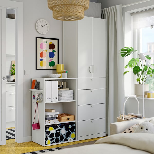 Moderne slaapkamer met een witte opslagruimte, planken, lades, kleurrijke decoratie en een grote plant.