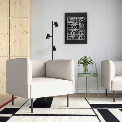 Moderne woonkamer met een witte LILLEHEM bank en bijzettafels. Versierd met een geometrisch tapijt, een kunstwerk en een groene kruk met bloemen.