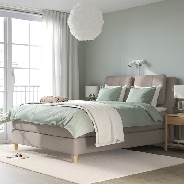 Moderne slaapkamer met grijs bed, groen beddengoed, groot raam en vloerkleed.