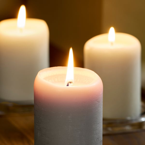 Drie brandende kaarsen in tinten wit, roze en grijs wierpen een knusse gloed op een houten oppervlak.