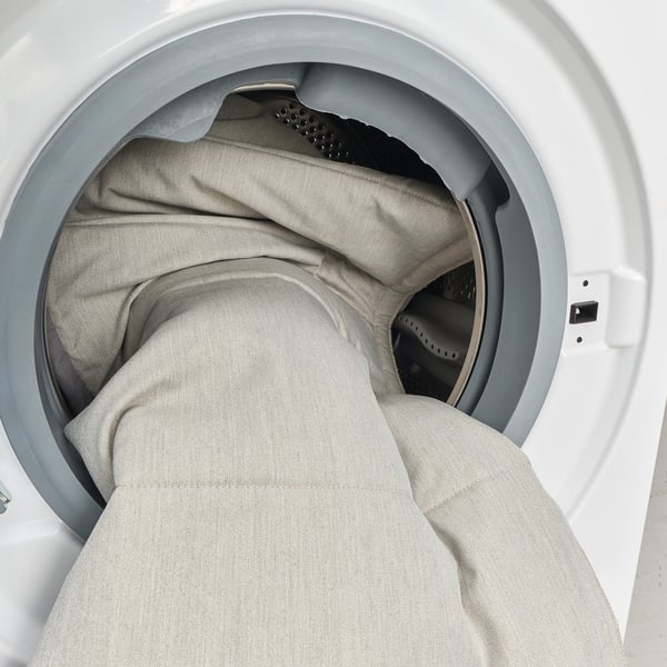 Witte wasmachine gevuld met opgevouwen grijze kleren.
