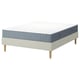 Een IKEA LYNGÖR bedbasis met een wit Valevåg-matras en beige bekleding. Het bed heeft lichte houten poten en een eenvoudig, modern ontwerp.