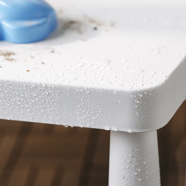 Waterdruppels parelen op de witte rand van de buitenkindertafel. Het blauwe voorwerp zit bovenop de tafel. Perfect voor picknicks.