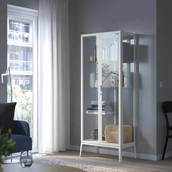 Witte vitrinekast met boeken en decor, in de buurt van een blauwe stoel, rustige kamer.