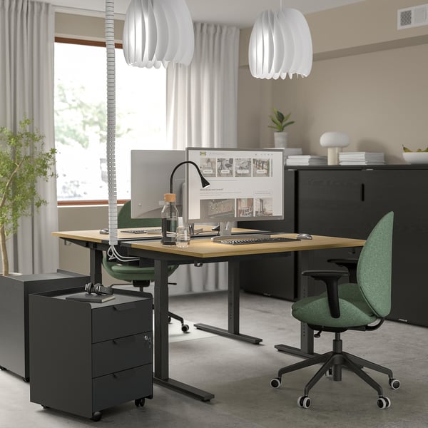 Verstelbaar bureau, groene stoel, groot scherm, hanglampen, zwarte kast - minimalistische kantooropstelling.