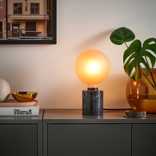 Moderne leefruimte met MOLNART lamp, ijzige bruine lamp op marmeren sokkel, geplaatst naast grote planten en decorartikelen.