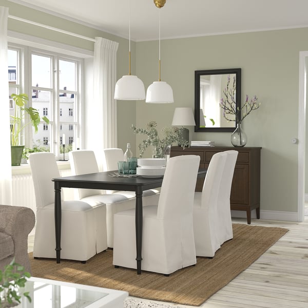 Moderne eetkamer met levendige lichten, zwarte tafel, witte stoelen, pluche bank en grote ramen.