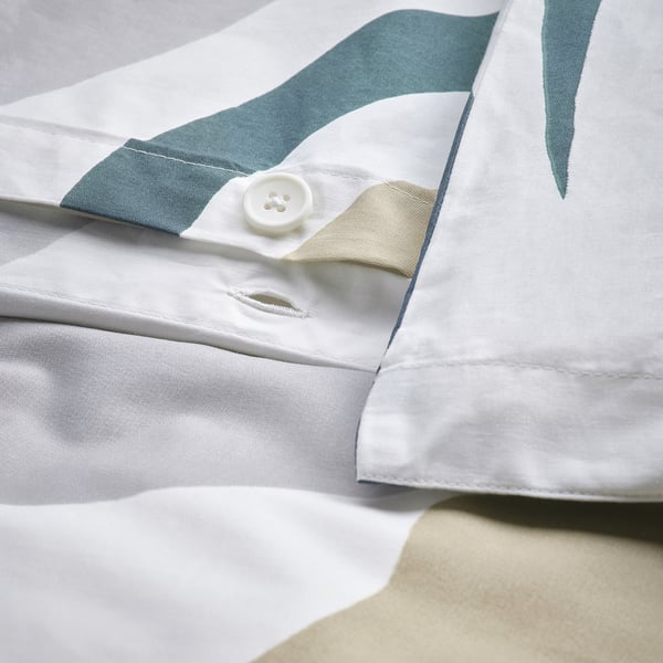Close-up van een dekbedovertrek met een knoopsluiting en groen bladpatroon, met draaddetail.