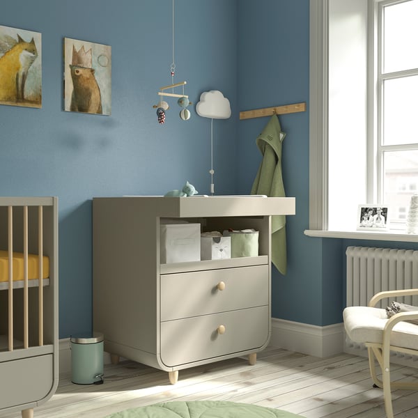 Lichtblauwe MYLLRA commode met lades, afneembaar front, tussen wieg en radiator.