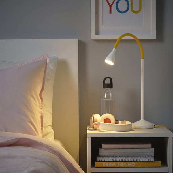 Slaapkamer met bed, gele NÄVLINGE lamp, waterfles en boeken.