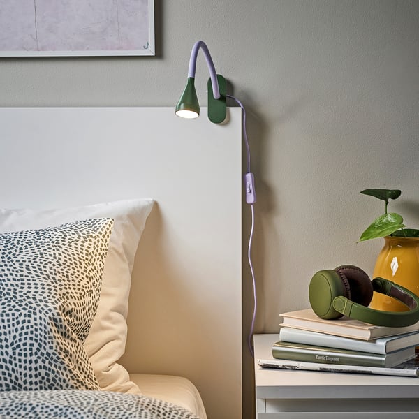 Gezellige slaapkamer met paars-groene lamp, nachtkastje boeken, koptelefoon, plant.