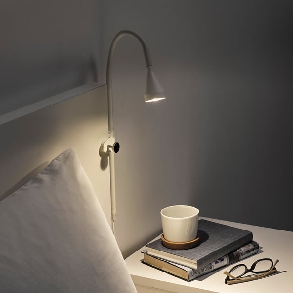Aan de muur gemonteerd verstelbaar licht met warme gloed op bedframe, naast kopje en boeken.