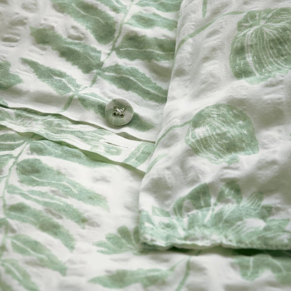Close-up van een groene, bladerige dekbedovertrek met knoopsluiting, getextureerde, lichte stof.