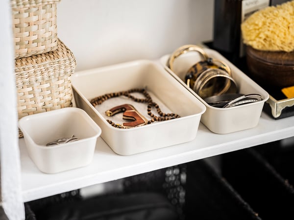 Witte georganiseerde plank met sieraden in doorzichtige plastic dozen, met kettingen, ringen en armbanden.