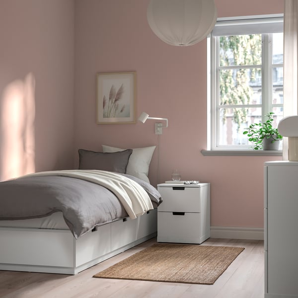 Kleine gezellige slaapkamer met NORDLI bed, grijs beddengoed, lichtroze muur, nachtkastje, plant en natuurlijk licht.
