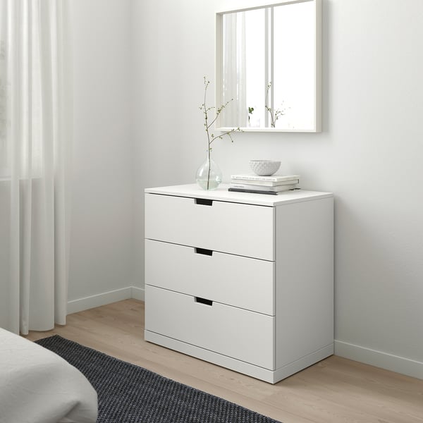 Witte NORDLI kist met 3 lades tegen de muur, strakke zwarte handgrepen, kom & vaas bovenop.