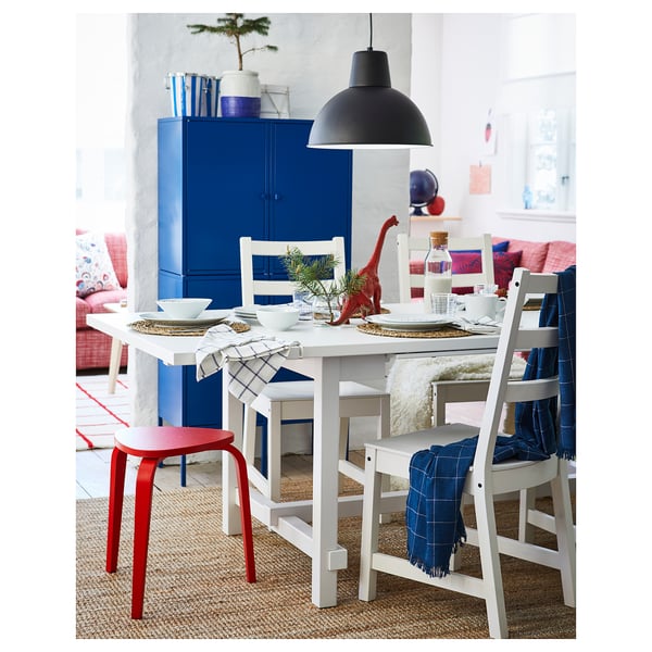 Eetkamer met uitschuifbare tafel, blauwe kast, witte stoelen, dinosaurusspeelgoed en zwarte hanglamp.