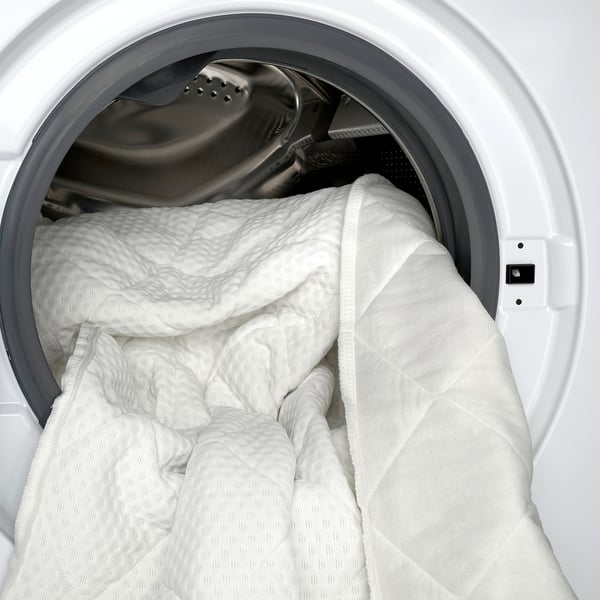 Witte matrastopper in een wasmachine, die laat zien hoe het wasbaar is.