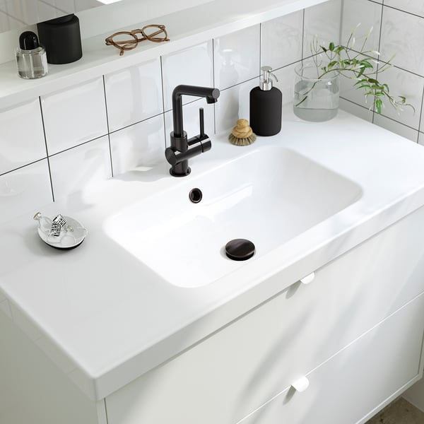 Moderne witte wastafel in de badkamer met strakke kraan, zeepdispenser en plant.