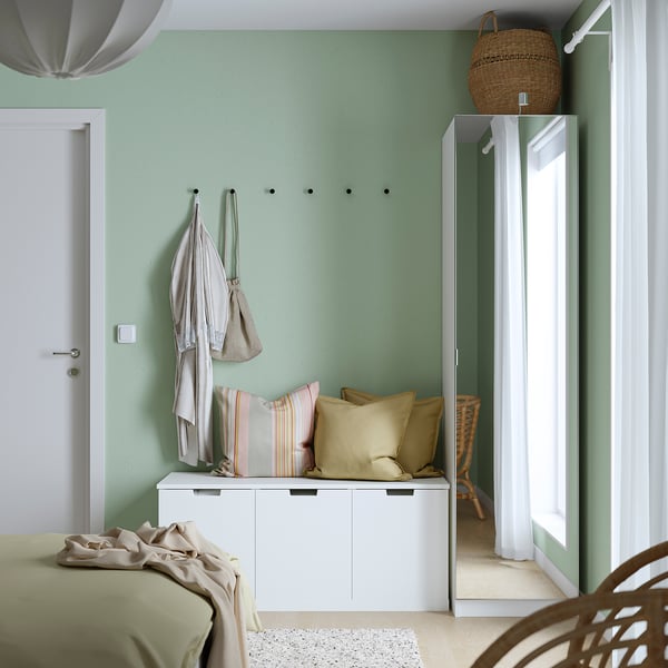 Moderne slaapkamer met witte PAX kledingkast, vitrage, lichte jassen, mand en bed met groene deken.
