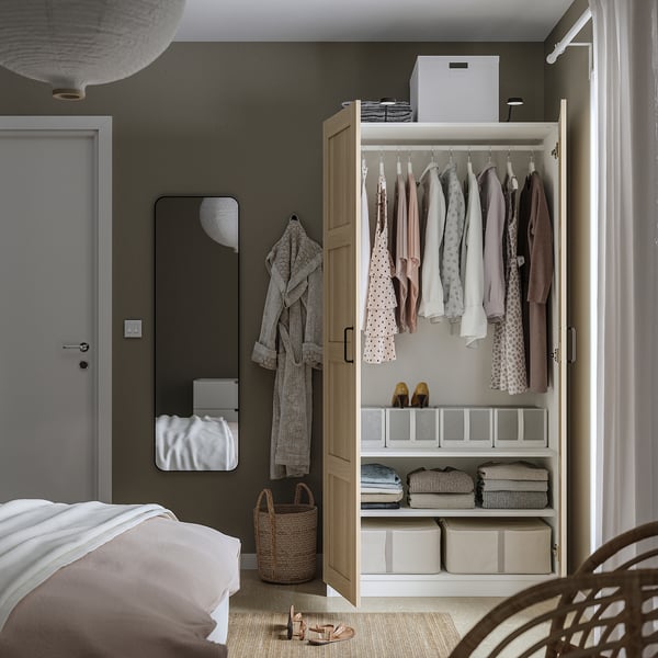 Open PAX kledingkast met kleerhangers, planken met opgevouwen kleding en dozen. Presentatie van georganiseerde opslag in een slaapkameromgeving.