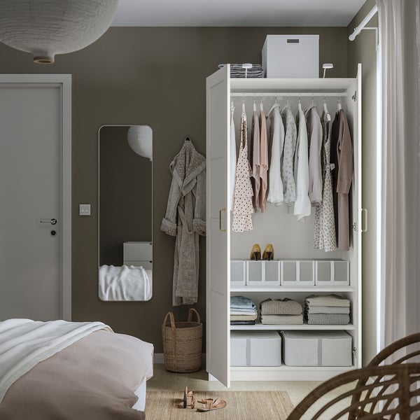 Goed georganiseerde slaapkamer met PAX kledingkast, voorzien van kleding, opgevouwen kleding en opbergdozen. Een spiegel en hangers zijn zichtbaar.