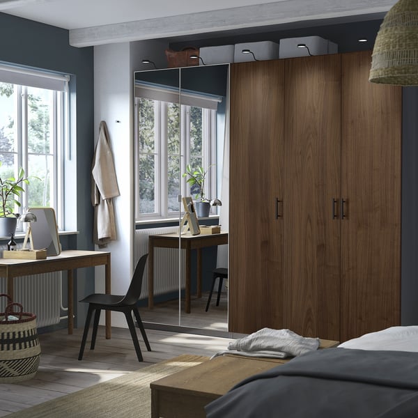 Moderne slaapkamer met grote PAX kledingkast in houtkleur, naast een bureau en zwarte stoel, voorzien van een spiegel en geweven textiel.