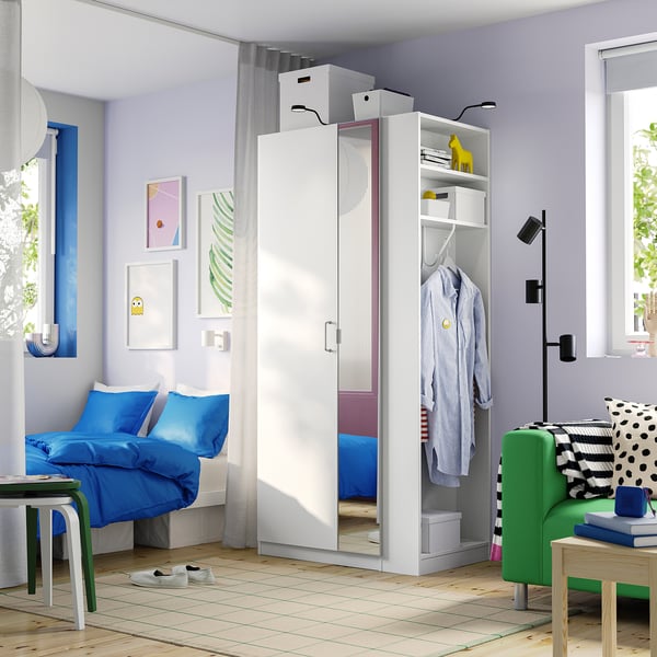 Moderne slaapkamer met witte PAX kledingkast, blauw beddengoed, groene stoel, houten vloer.