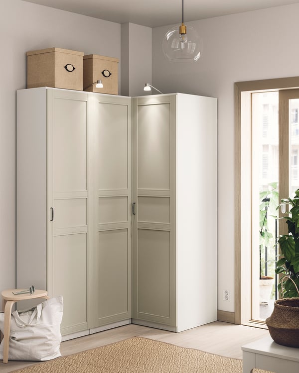 Een moderne hoekkast, genaamd PAX, lichtbeige kleur, met strak design met meerdere planken voor opslag. Daarboven is een hanglamp geplaatst.