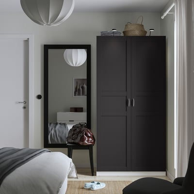 Moderne slaapkamer met zwarte PAX kledingkast, spiegel, bed en manden. Witte hanglampen, grijs vloerkleed en sandalen.