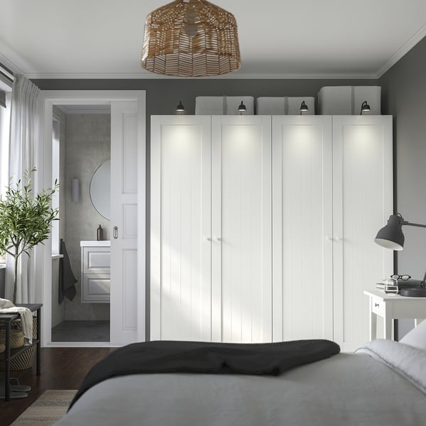 Moderne slaapkamer met grote PAX kledingkast, donker bed, zwarte lamp en kleine badkamer.