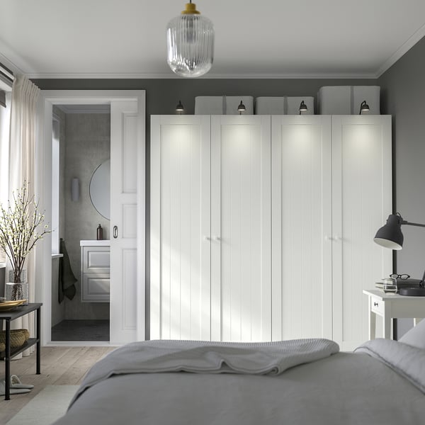Moderne slaapkamer met grote witte kledingkast, grijze muren, houten vloer en bed. Kledingkast heeft geïntegreerde verlichting. Uitzicht op de badkamer door open deur.