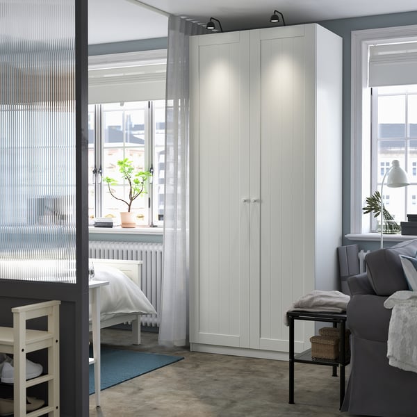 Moderne kamer met hoge witte kledingkast, stoel en plant.