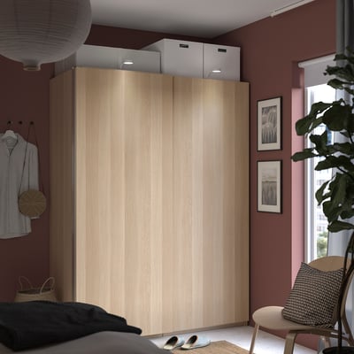 Moderne slaapkamer met PAX beige kledingkast, witte dozen, groene plant, zwart-witte kussens, gestreept overhemd en kunstlijsten.