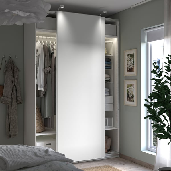 Slaapkamer met open witte PAX-kledingkast die kleding, planken en opslag onthult; Grijze muren en raam met plant.