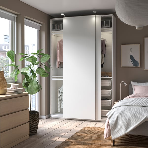 Een moderne, witte schuifdeurkast in een slaapkamer. Hanglamp, grote plant, bed en breed raam met uitzicht.