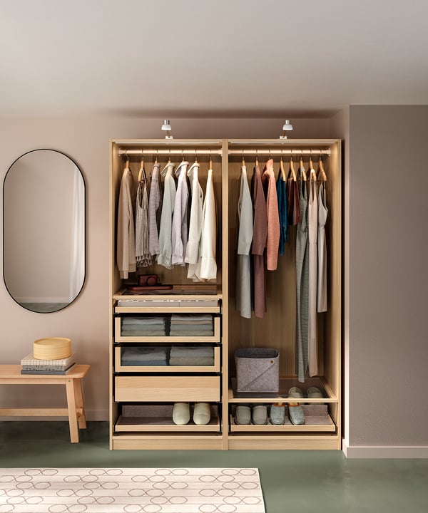Open houten PAX kledingkast, hangende kleding, laden, & accessoires. Lichtbeige wanden, groene vloer, ronde spiegel.