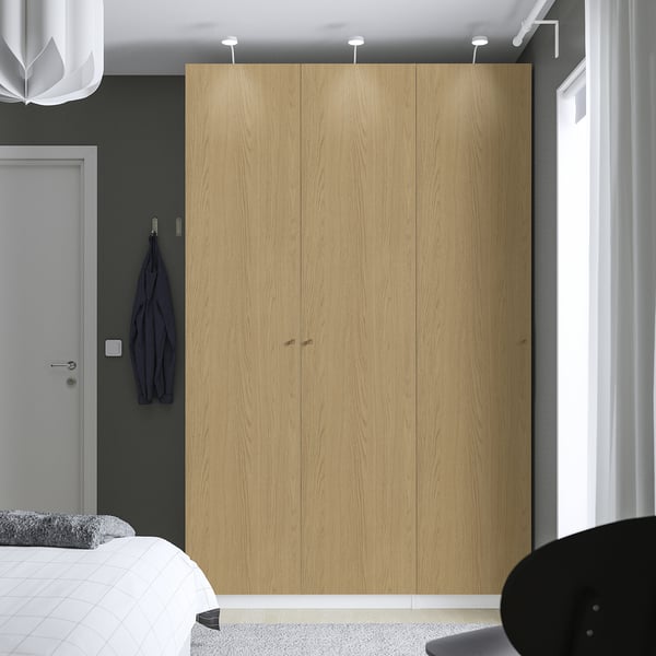 Moderne slaapkamer met grote lichthouten PAX kledingkast, grijze muur, hangend jasje en gedeeltelijk zichtbaar bed.