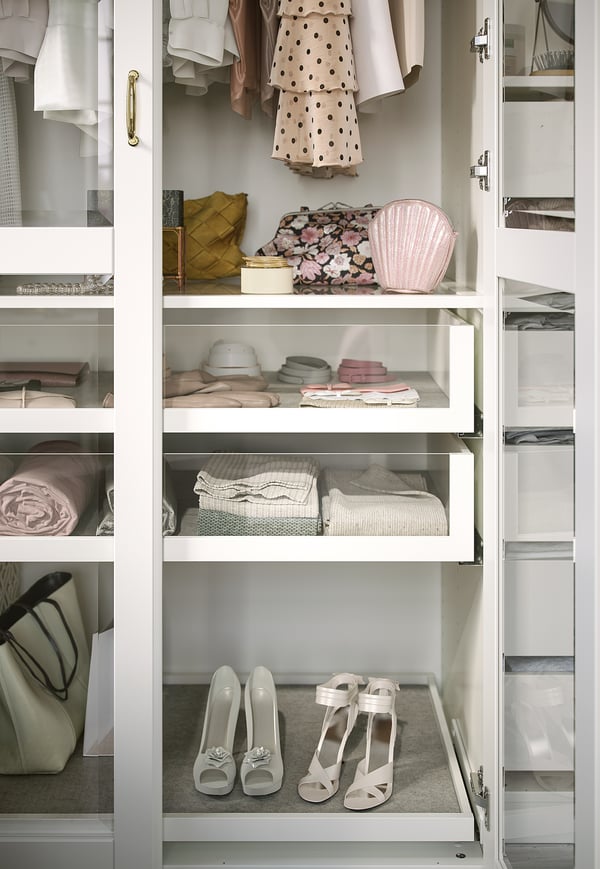 Een witte kledingkast met glazen planken toont netjes georganiseerde kleding en accessoires.