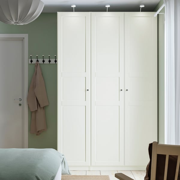 Minimalistische slaapkamer met PAX kledingkast, lichtgroene wanden. Kledingkast hoog, wit, past bij de deur. Kledingroede zichtbaar.