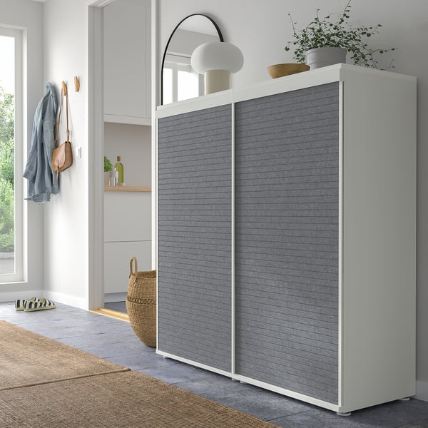Moderne kast met grijze schuifdeuren, wit frame. Gedecoreerd met planten, lamp en spiegel. Groot, staat bij een raam.