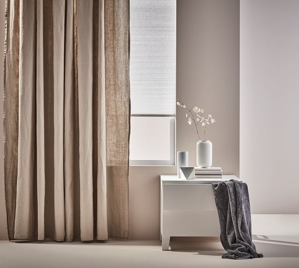 Minimalistisch woongedeelte met beige gordijnen, grijze console, witte vaas met takken en gedrapeerde plaid.