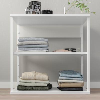 Witte PLATSA kast met opgevouwen kleding, cameradisplay en plant.