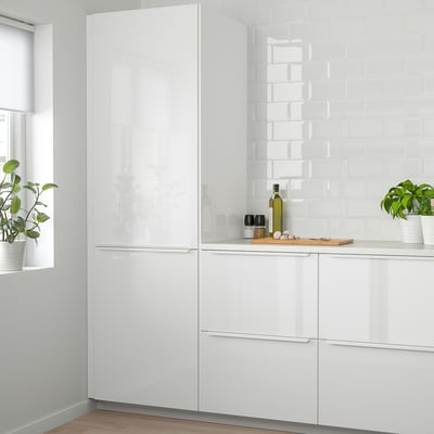 Moderne witte keuken met glanzende kasten. Glanzende lades en hoge kasten hoger dan het raam. Groene planten op aanrecht.