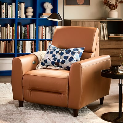 Moderne beige leren relaxstoel met een gestippelde kussen, naast de boekenkast en het bijzettafeltje.